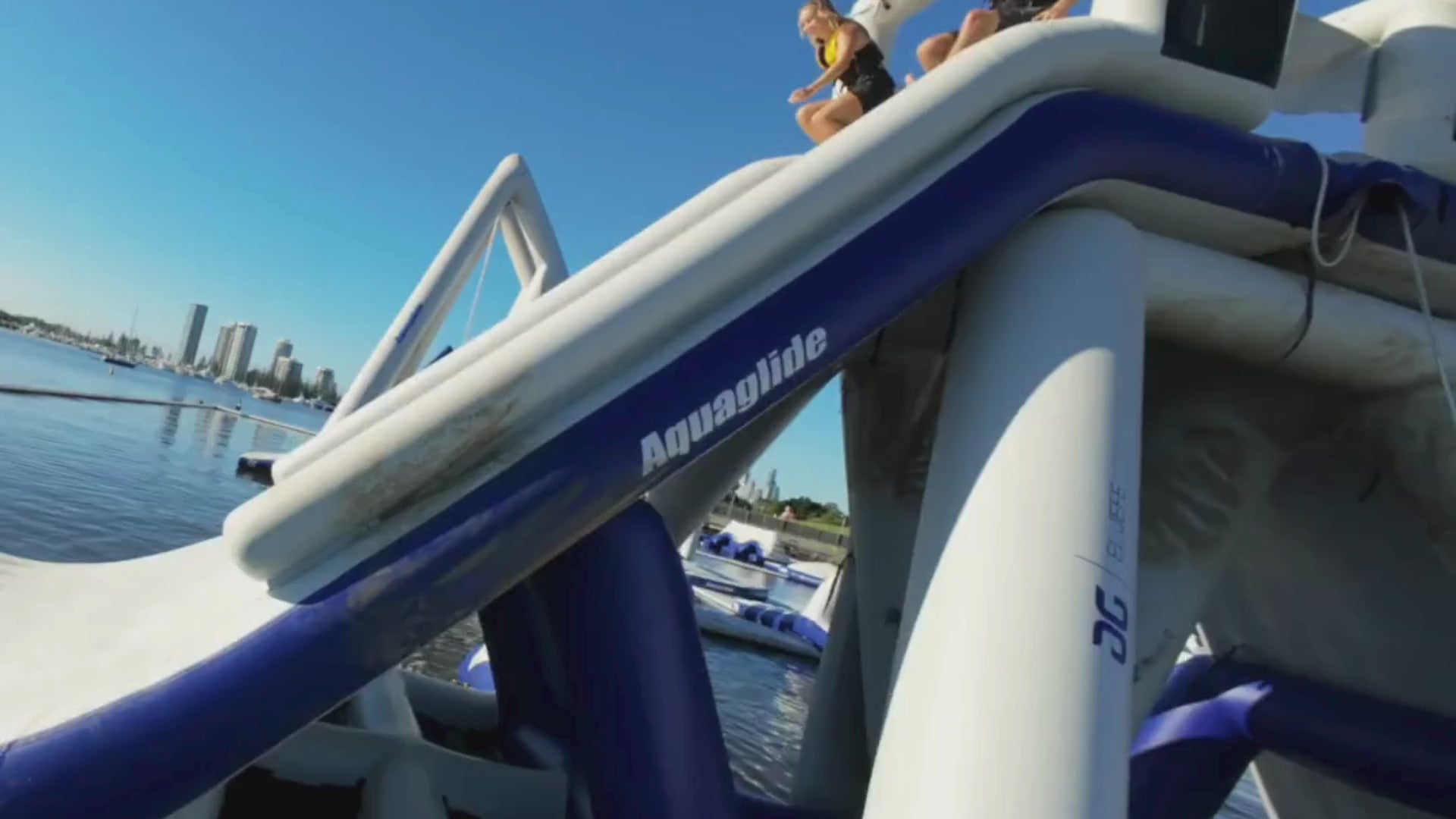 Video of a young man and young woman enjoying an inflatable water park slide by Water Warrior Services, showcasing floating obstacle courses and slides on the water.